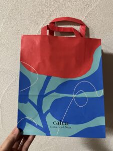 赤とブルーの大胆な花柄が描かれたcaicaの紙バッグ